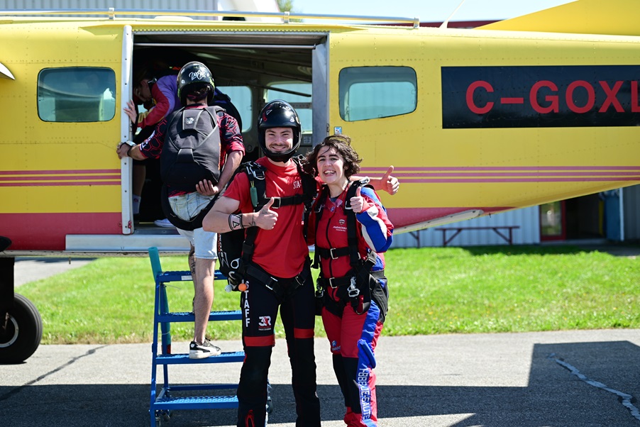 Myriam est en compagnie de son instructeur de saut, et se prépare à monter dans un avion jaune.