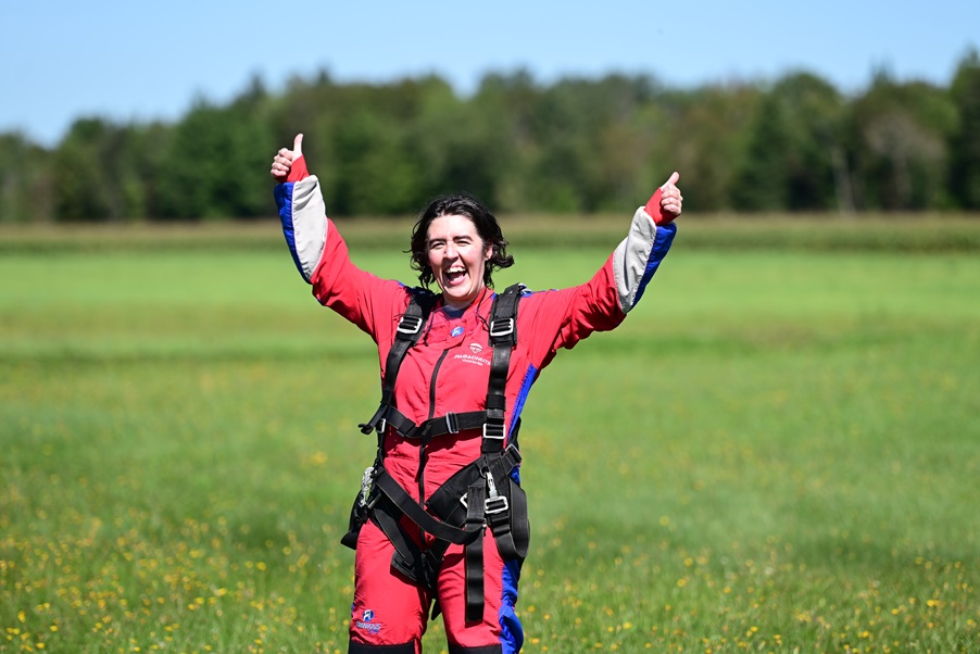 Myriam, en combinaison de parachutiste, lève les pouces dans les airs avec un sourire fier.
